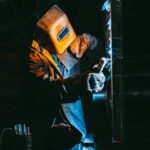 Lead Lined Drywall A welder wearing safety gear sparks metal in a dimly lit industrial setting.